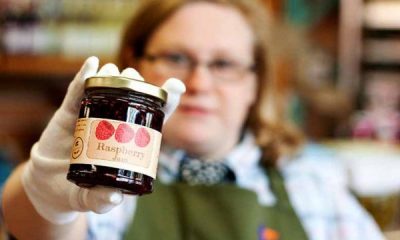 A woman in an apron hold out a jar of Raspberry Jam